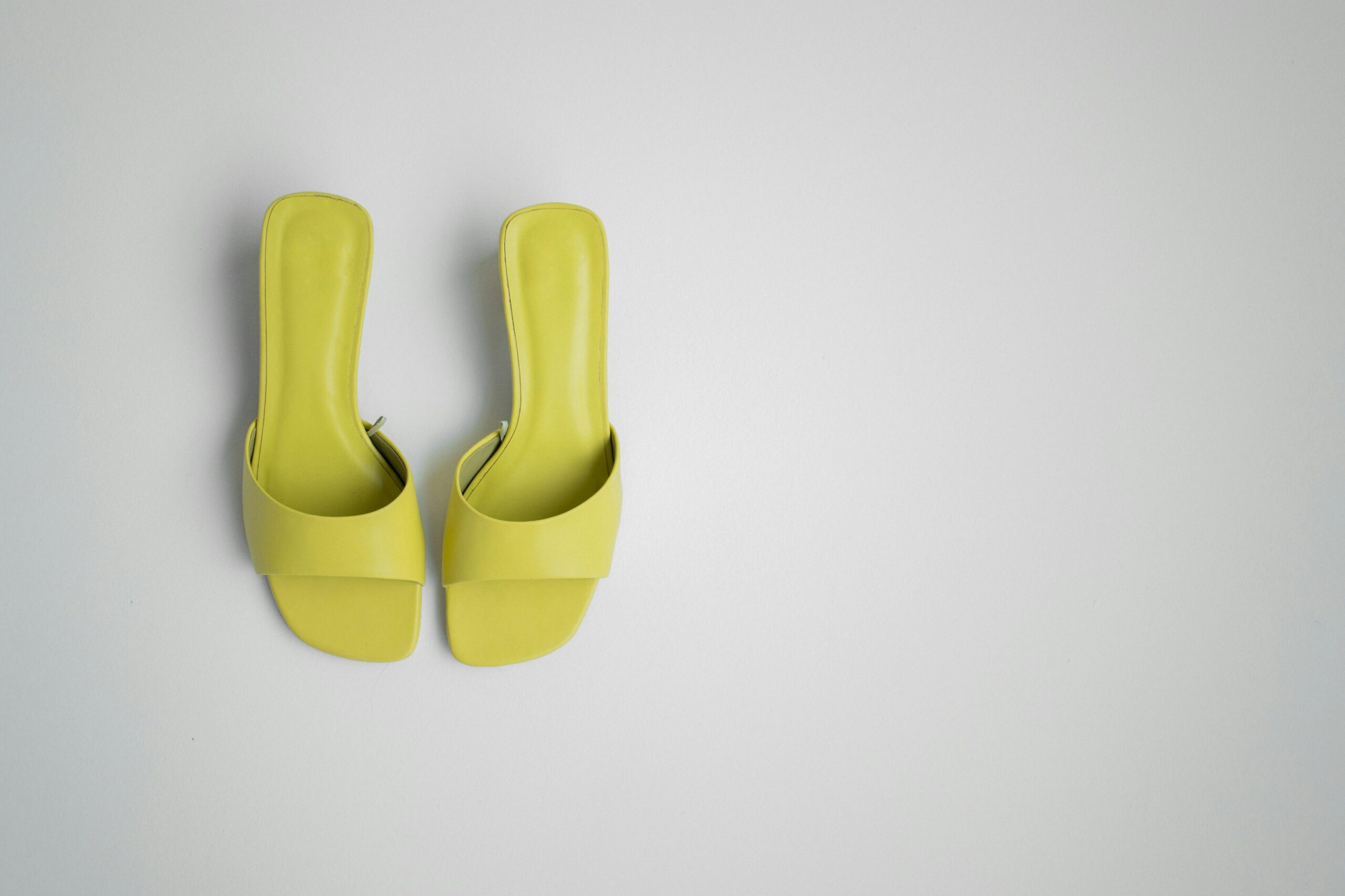 Chic neon yellow mules placed on a light background, showcasing modern footwear style.